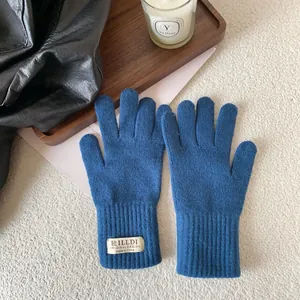 Close-up of navy knit gloves with long ribbed cuffs and brand tag on a cozy tray