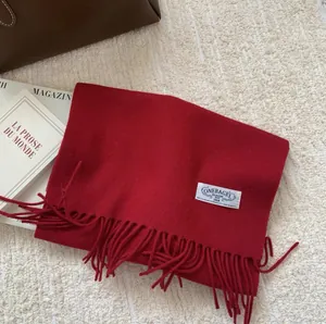 Détail de l'écharpe en laine rouge avec franges et étiquette sur tapis texturé