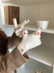 Macro shot of cream knitted gloves featuring flip-top fingers and red smiley face embroidery