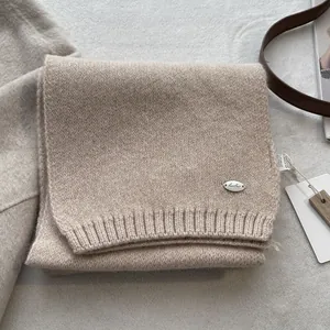 Detailed close-up of oatmeal wool blend knit scarf with metallic brand tag and soft texture