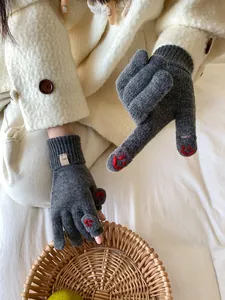 Detail of dark grey knitted gloves with red smiley face embroidery and thumb opening