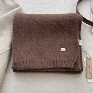 Detail of soft dark brown wool knit scarf with silver metal logo and wooden tag