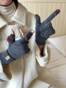Detail view of dark grey knitted gloves with red smiley face embroidery and logo tag