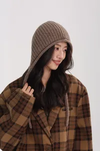 Detail of wool knit hat with brown plaid coat and embroidered sleeve text