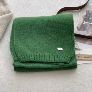 Detail of grass green wool knit scarf with silver logo plate and ribbed finish texture