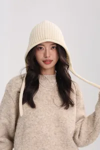 Detail of cream wool knit hat with ear flaps and ribbons paired with a beige sweater