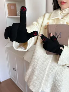 Close-up of black knitted gloves with red smiley face embroidery held with a book