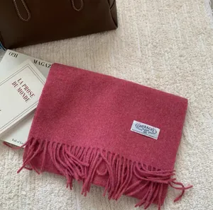 Détail d'une écharpe en laine rose foncé à franges sur tapis blanc avec sac en cuir et magazine