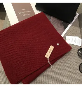 Close-up of a red ribbed knit winter scarf with a decorative brand tag and metal logo