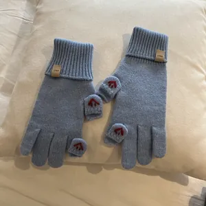 Detail of light blue knit gloves featuring red finger embroidery and a branded ERET woven label