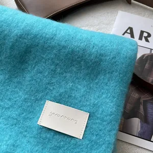 Detail of teal wool scarf texture with leather brand tag on magazine background