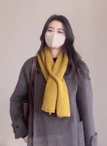 Détails de la texture du foulard en laine jaune évidé porté avec un long manteau gris