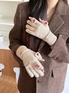 Detail of beige knitted fingerless gloves with red flower embroidery and branded wrist tag