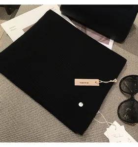 Close-up of black ribbed knit scarf with branded tags and natural camphor wood charm