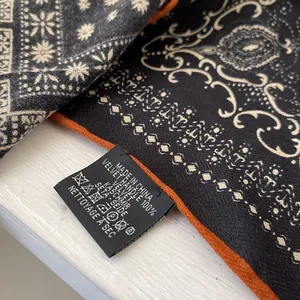 Detailed close-up of a paisley silk and wool blend scarf with washing label and orange edge