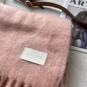 Close-up of soft pink cashmere scarf showing fuzzy texture, fringe edge, and white leather tag