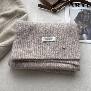 Detail of wool-blend oatmeal knitted scarf featuring a white woven label and metal buckle