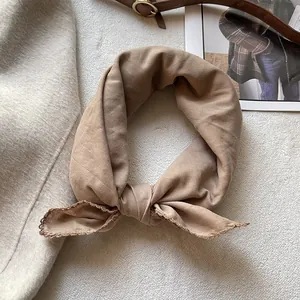 Dettaglio di un foulard in cotone marrone chiaro con bordo in pizzo su un tappeto morbido