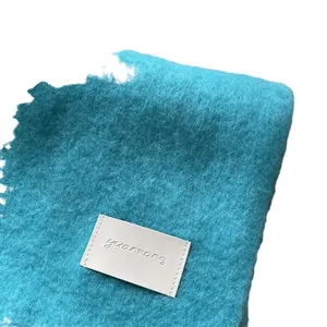 Soft blue-green wool scarf with a leather logo label, showing a warm fuzzy texture