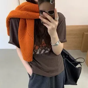 Détail d'une écharpe en laine tricotée ajourée orange vif sur un t-shirt marron foncé