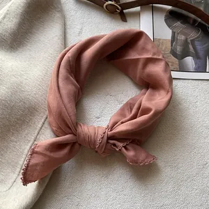 Dettaglio del foulard in cotone rosa polvere con pizzo all'uncinetto su lana beige