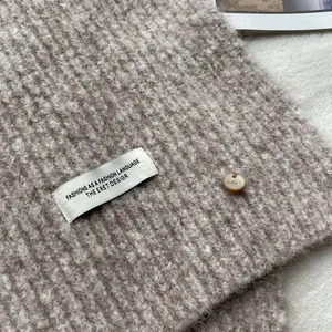 Detail shot of oatmeal wool blend scarf showing soft knitted texture and brand label