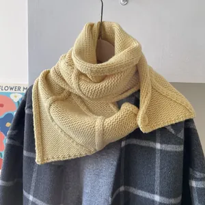 Détail d'écharpe en laine tricotée jaune clair avec bouton sur manteau gris