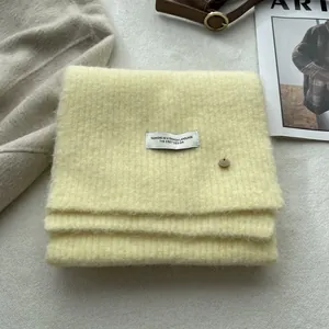 Detail of soft beige wool knit scarf featuring vertical ribbed texture and woven label
