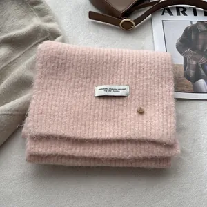 Detail of pink knitted wool scarf with ribbed texture, fabric label and golden button