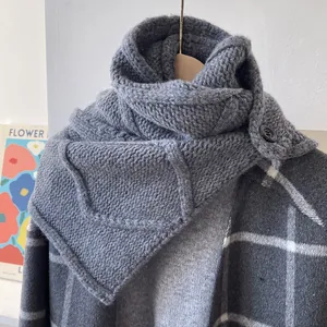 Détail d'une écharpe en laine grise à grosses mailles avec bouton noir sur un manteau chic