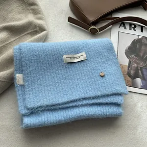 Close-up of light blue wool knit scarf with fashion label and gold metal detail
