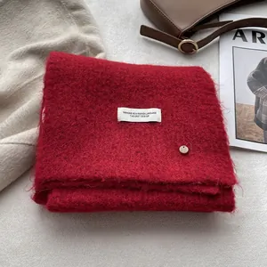 Close-up of red wool-blend scarf with a white label and a small golden metal charm