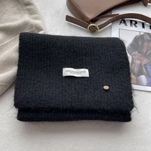 Detail of soft black wool knit scarf featuring white woven label and brown button detail