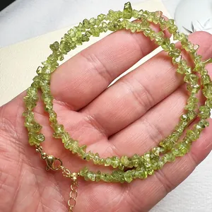 Détail du collier en perles de péridot naturel avec fermoir mousqueton doré en main