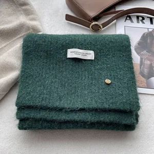 Close-up of wool knit scarf in forest green with decorative label and button detail