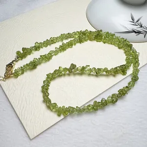 Détail du collier en perles de péridot naturel avec fermoir doré sur papier blanc