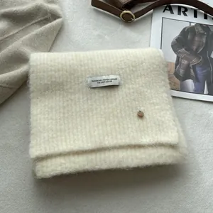 Detail of cream wool knit scarf featuring a branded fabric label and metal button detail