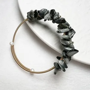 Détail d'un bracelet en pierres grises, perles blanches et fil doré sur plateau blanc