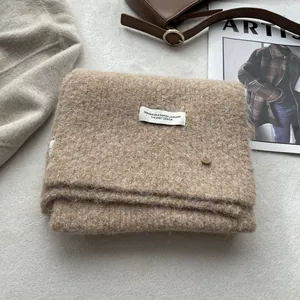 Detail of oatmeal wool scarf featuring a soft plush texture and minimalist brand label