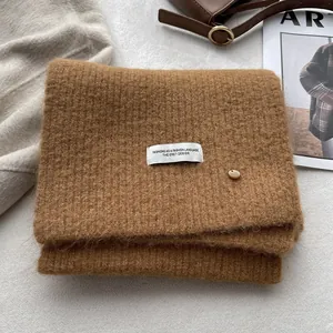 Macro detail of soft brown wool-blend knitted scarf with woven label and gold metal buckle