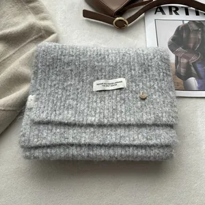 Detail of gray wool knit scarf showing soft texture, brand label and metal button ornament