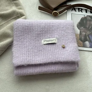 Detail of light purple wool knit scarf showing soft texture, white label, and metal button