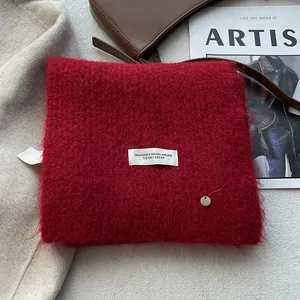 Detail of red mohair wool scarf featuring a white woven label and metal charm detail