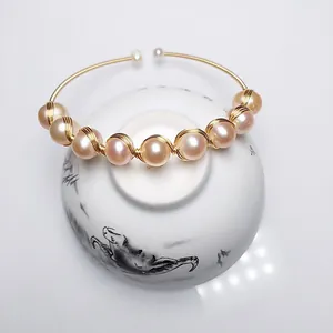 Detail of 14K gold-wrapped freshwater pink pearl bangle on a white ceramic display