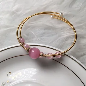 Detail of pink cat eye stone bracelet with gold wire wrap design and pearl accents