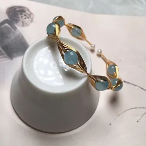Macro detail of gold wire-wrapped bangle with aquamarine stones and white pearls on a cup