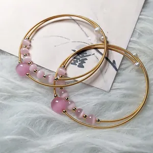 Close-up of pink cat eye stone beads and 14K gold wire layered bracelets on plush background