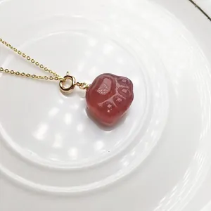 Detail view of a translucent red strawberry quartz cat paw pendant on a gold chain