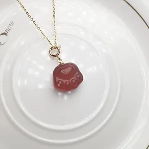 Macro shot of red strawberry crystal cat paw pendant on a gold chain over ceramic