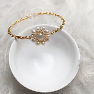 Macro view of a 14K gold-filled wire cuff featuring a pearl petal cluster on a ceramic bowl